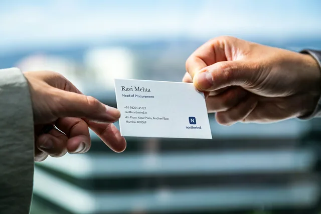 Two hands exchanging a business card (card details replaced with fictional ones)